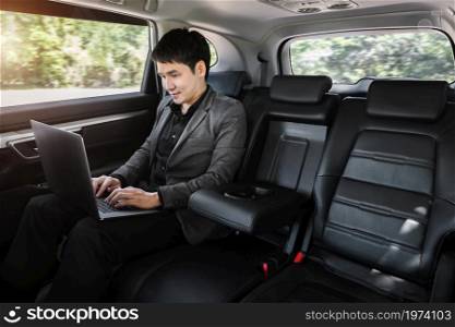 young business man using laptop computer while sitting in the back seat of car