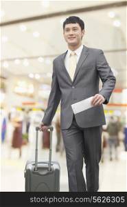 Young business man walking with suitcase and holding flight ticket in airport