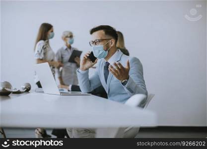 Young business man with medical protective mask works on a laptop and using mobile phone in the office