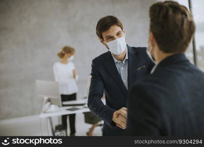 Young business men handshaking in the office with protective facial masks as a protection from coronavirus