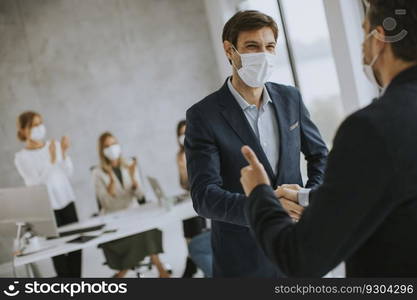 Young business men handshaking in the office with protective facial masks as a protection from coronavirus