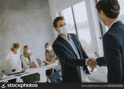 Young business men handshaking in the office with protective facial masks as a protection from coronavirus