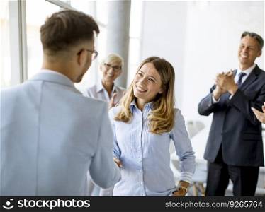 Young business partners making handshake in an office while their team applauding in the background