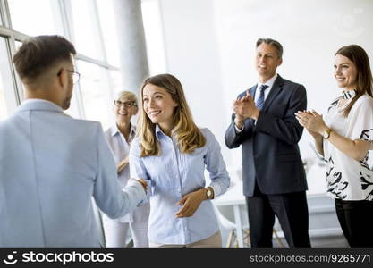 Young business partners making handshake in an office while their team applauding in the background