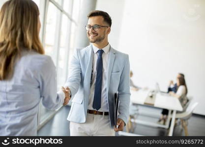 Young business partners making handshake in an office while their team working in the background