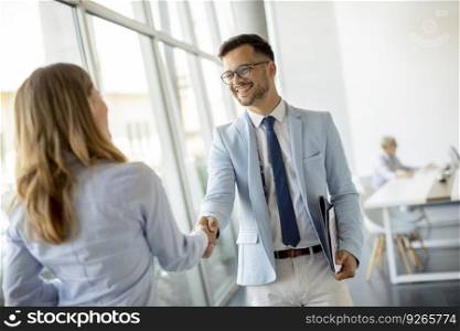 Young business partners making handshake in an office while their team working in the background