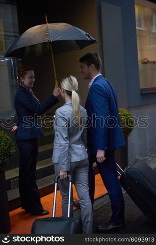 Young business people couple entering city hotel, looking for room, holding suitcases while walking on street