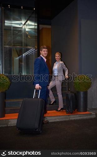 Young business people couple entering city hotel, looking for room, holding suitcases while walking on street