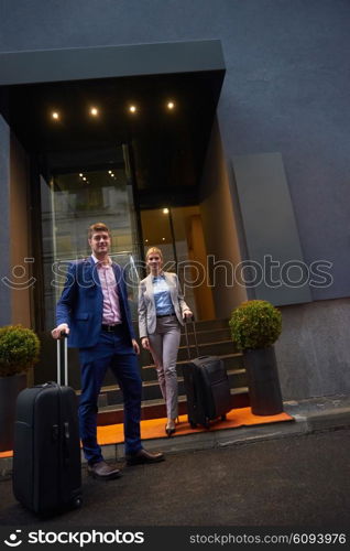 Young business people couple entering city hotel, looking for room, holding suitcases while walking on street