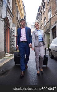 Young business people couple entering city hotel, looking for room, holding suitcases while walking on street