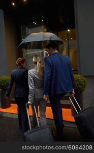 Young business people couple entering city hotel, looking for room, holding suitcases while walking on street