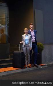 Young business people couple entering city hotel, looking for room, holding suitcases while walking on street