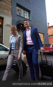 Young business people couple entering city hotel, looking for room, holding suitcases while walking on street