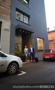 Young business people couple entering city hotel, looking for room, holding suitcases while walking on street