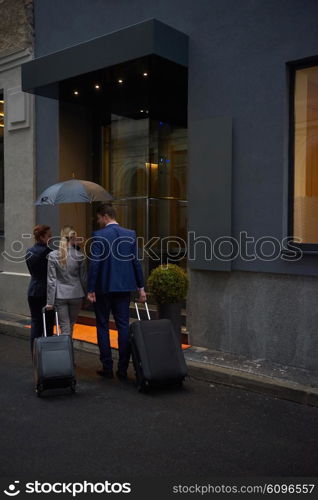 Young business people couple entering city hotel, looking for room, holding suitcases while walking on street