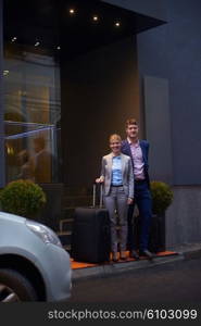 Young business people couple entering city hotel, looking for room, holding suitcases while walking on street