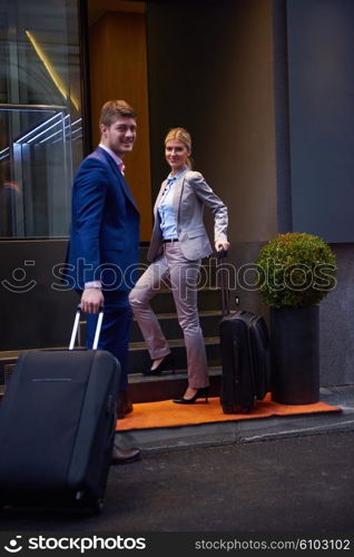 Young business people couple entering city hotel, looking for room, holding suitcases while walking on street