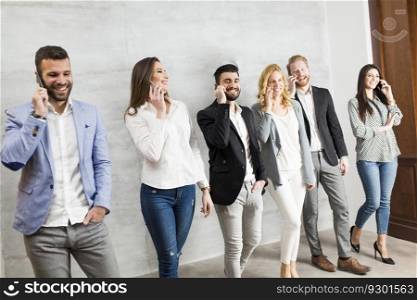 Young business people with mobile phone standing by the wall