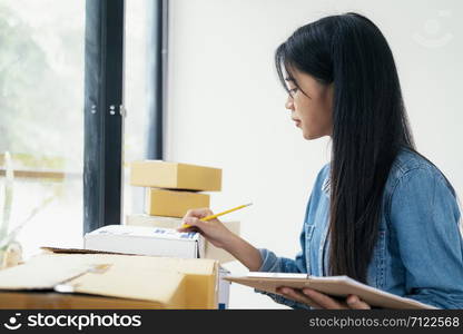 Young business startup online seller owner using computer for checking the customer orders from email or website and preparing packages for product office equipment.