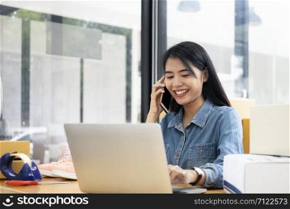Young business startup online seller owner using computer for checking the customer orders from email or website and preparing packages for product office equipment.
