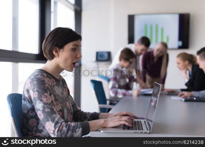 young business woman at modern startup office interior working on laptop computer, blured team in meeting, people group in background