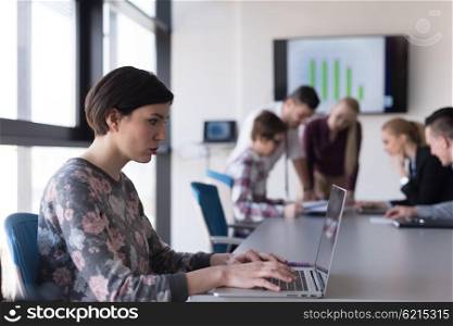 young business woman at modern startup office interior working on laptop computer, blured team in meeting, people group in background