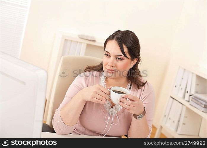 Young business woman enjoying coffee at modern office sitting at computer