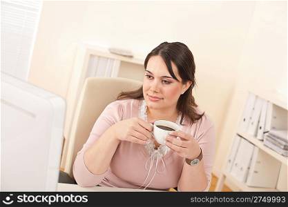 Young business woman enjoying coffee at modern office sitting at computer