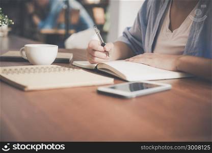 Young business woman in white dress sitting at table in cafe and writing in notebook. Asian woman talking smartphone and cup of coffee. Freelancer working in coffee shop. Vintage effect style pictures
