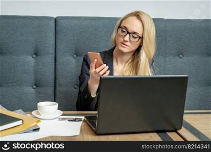Young business woman is using smartphone sitting at table in cafe.. Woman is reading message on her cellphone.