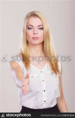 Young business woman making welcome invitating hand sign gesture or giving palm for handshake. Studio shot on gray