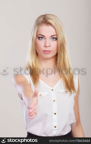 Young business woman making welcome invitating hand sign gesture or giving palm for handshake. Studio shot on gray