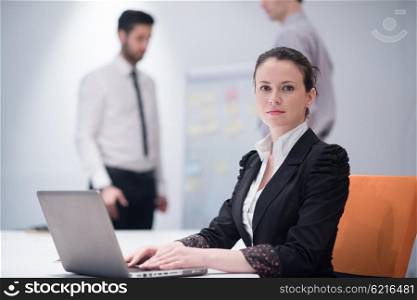 young business woman on meeting usineg laptop computer, blured group of people in background at modern bright startup office interior taking notes on white flip board and brainstorming about plans and ideas