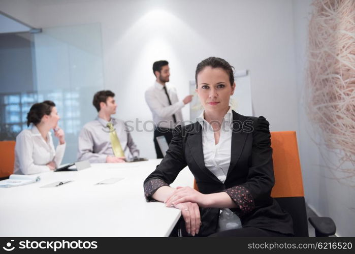 young business woman on meeting usineg laptop computer, blured group of people in background at modern bright startup office interior taking notes on white flip board and brainstorming about plans and ideas