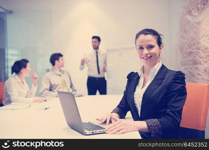 young business woman on meeting usineg laptop computer, blured group of people in background at modern bright startup office interior taking notes on white flip board and brainstorming about plans and ideas