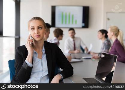 young business woman speaking on phone at modern startup office interior, team in meeting group in background