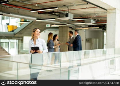 Young business woman standing with digital tablet in the office hallway