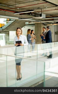 Young business woman standing with digital tablet in the office hallway