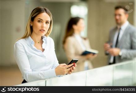 Young business woman standing with mobile phone in the office hallway