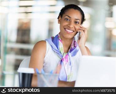 Young business woman talking over phone in front of her laptop
