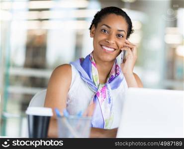 Young business woman talking over phone in front of her laptop