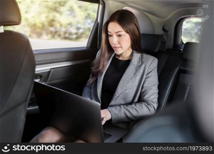 young business woman using laptop computer while sitting in the back seat of car