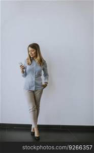 Young business woman using mobile phone by the wall in the office