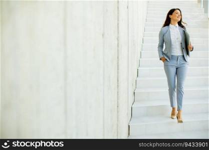 Young business woman walking down the stairs and holding laptop at the office hallway