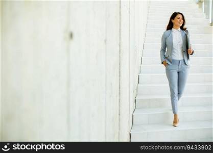 Young business woman walking down the stairs and holding laptop at the office hallway