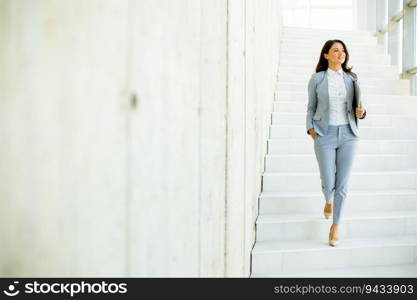 Young business woman walking down the stairs and holding laptop at the office hallway