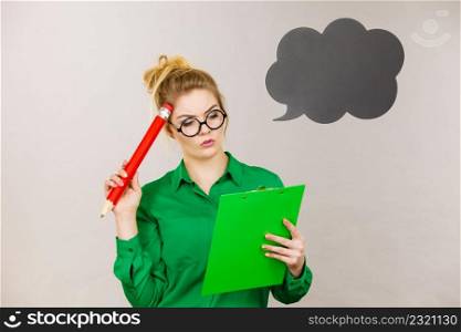 Young business woman wearing jacket intensive thinking finding great problem solution and ideas writing something down in note, black speech bubble next to her. Business woman intensive thinking and writing