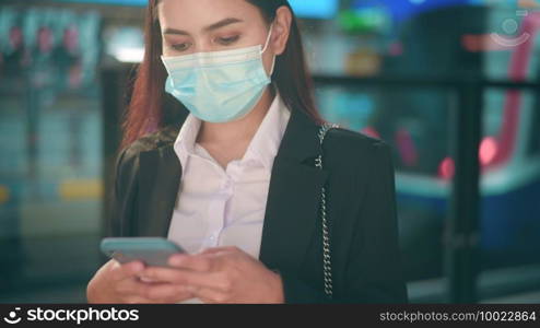 Young business woman with face mask is standing on metro platform using smart.  
