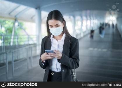 Young business woman with face mask  is standing on metro platform using smart. 