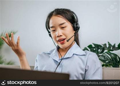 Young business woman working on computer, talking online using a headset while sitting on the comfortable sofa at home. Concept of remote work from home